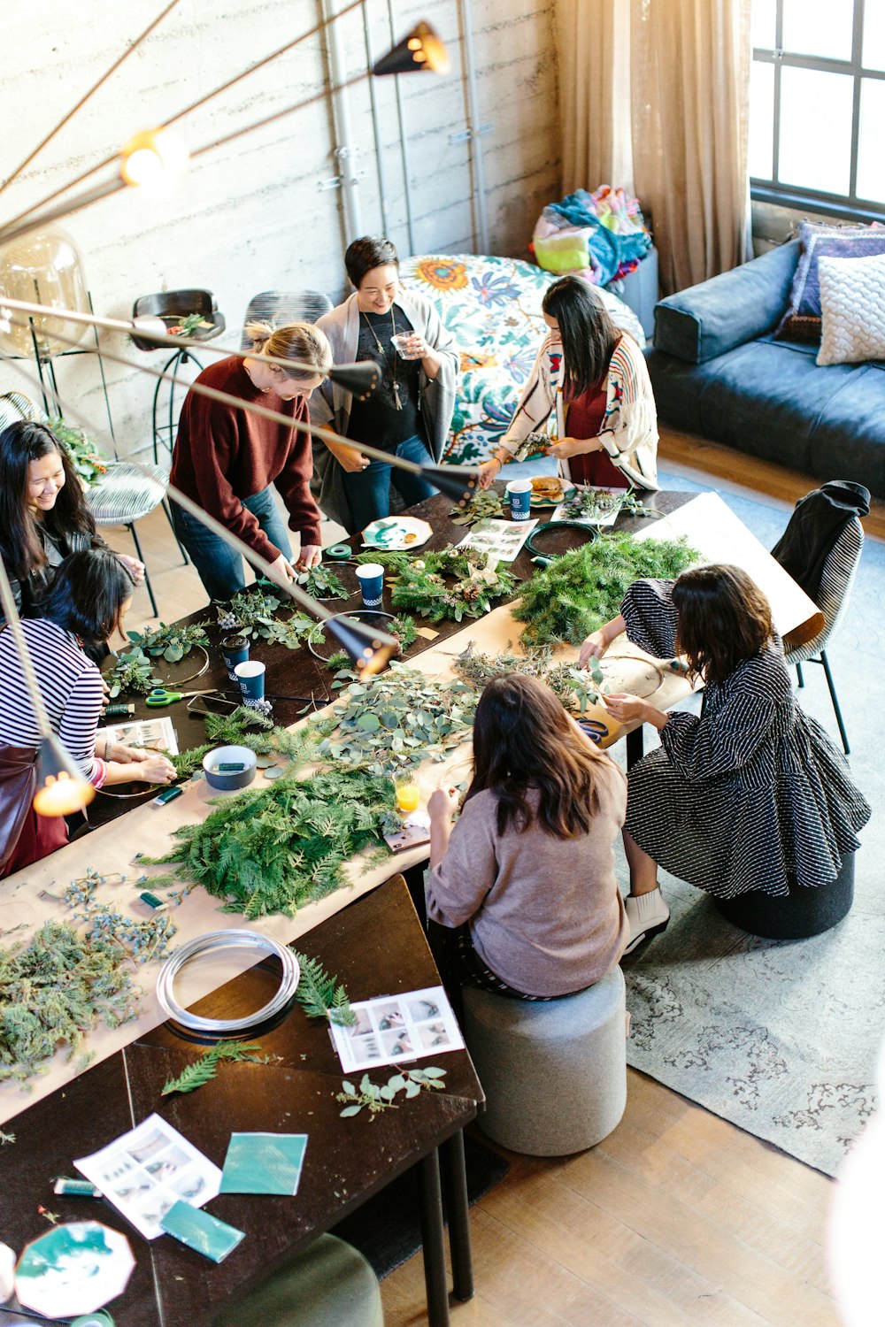 A group crafting with fresh greenery around a long workshop table
