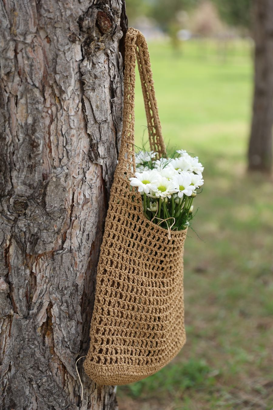 Woven jute bag hanging on a tree trunk with daisies
